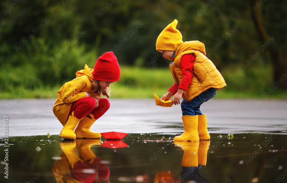 快乐的孩子女孩和男孩在秋天的水坑里用纸船在大自然中。