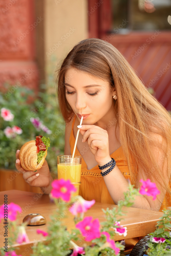 女人在户外咖啡馆吃美味的羊角面包喝果汁