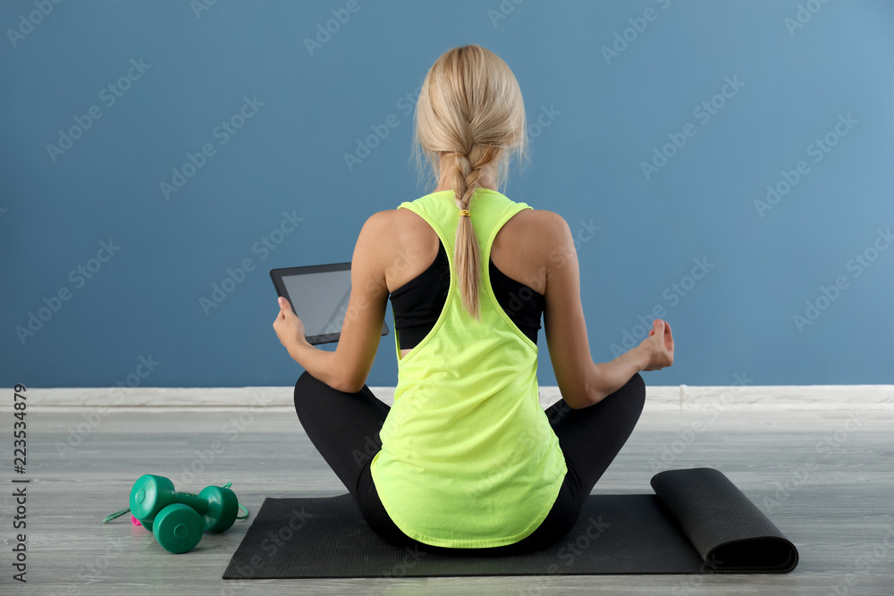年轻女性拿着平板电脑坐在室内瑜伽垫上。休息和工作之间的平衡概念