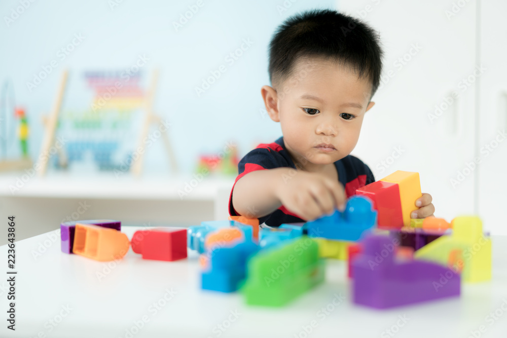 可爱的亚洲幼童坐在椅子上，在家里玩色块玩具。