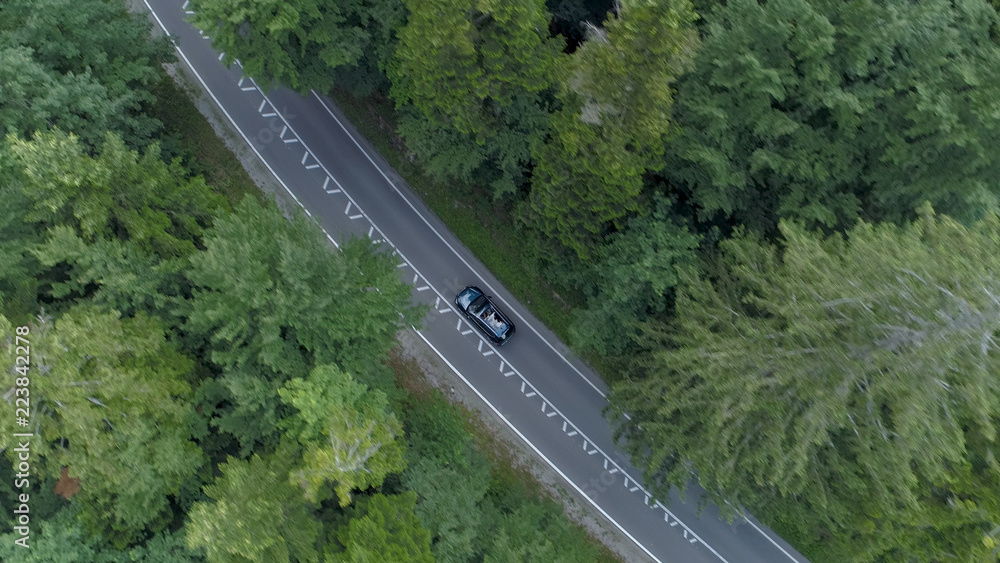 空中飞行：在一辆黑色汽车上方飞行，沿着空旷的道路行驶，穿过森林。