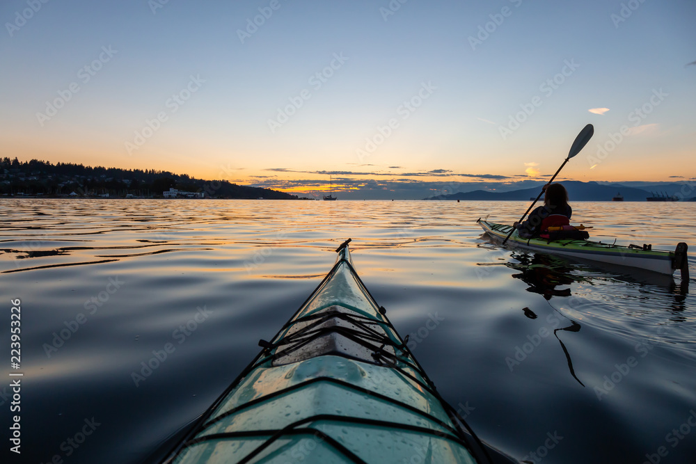 在充满活力的阳光明媚的夏季日落中，女孩海上皮划艇。拍摄于加拿大不列颠哥伦比亚省温哥华市。