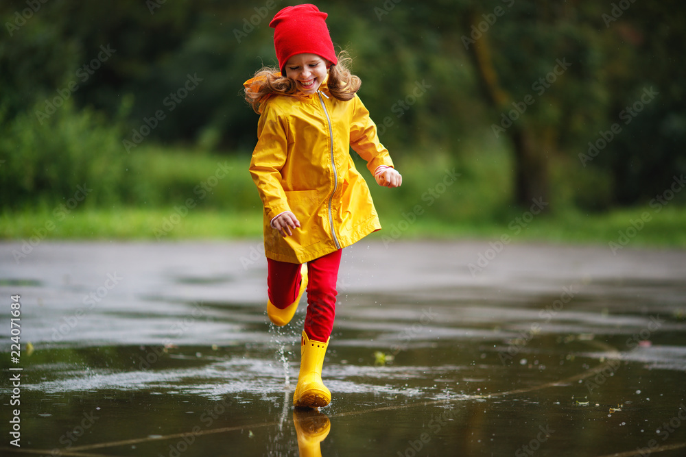 快乐的小女孩穿着橡胶靴在水坑里跑秋天的路