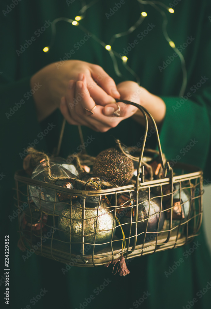 绿衣女子手中装满圣诞或新年树复古装饰玩具的铁丝篮