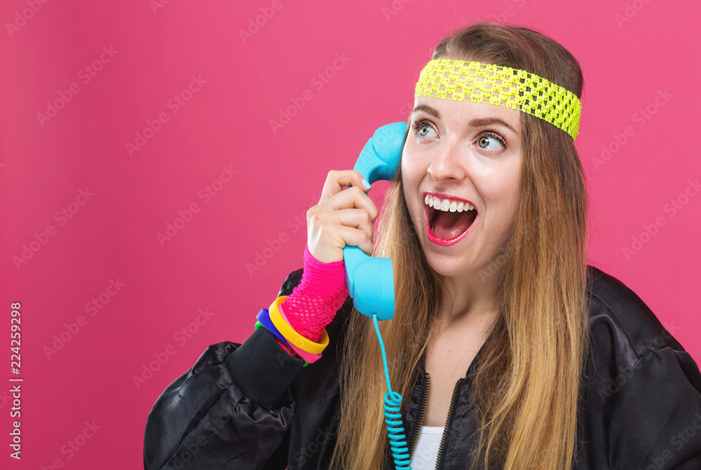 80年代时尚的女人，粉色背景下的老式手机