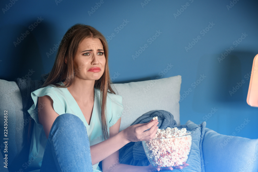情绪激动的年轻女子在家看电视时吃爆米花