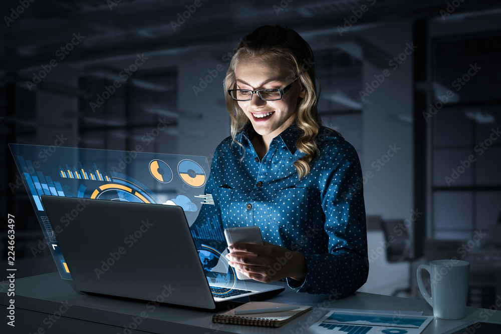漂亮的金发女郎在笔记本电脑和屏幕外的信息图上工作。