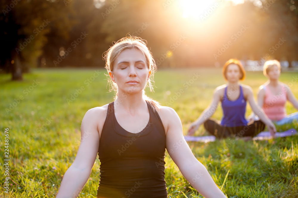 公园里的瑜伽，一群混合年龄的女性在日落时练习瑜伽和冥想