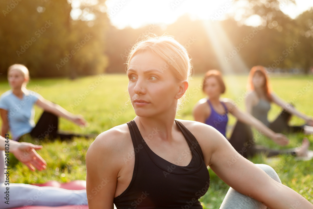 Yoga in the park, middle age woman doing exercises with group of mixed age people