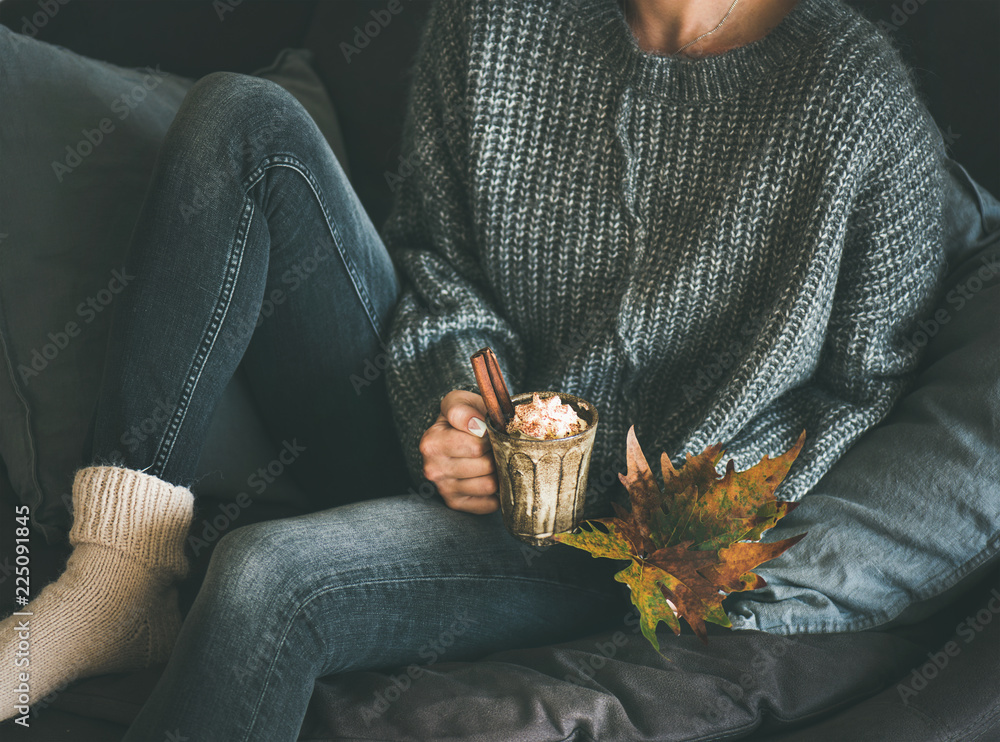 穿着羊毛衫和牛仔裤的女人坐着，手里拿着一个盛着热巧克力或生咖啡的杯子
