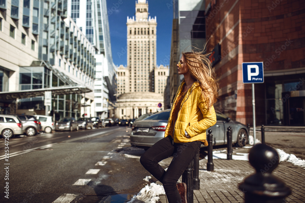 一位年轻的欧洲女性，旅行时留着金色长发，穿着黄色夹克，戴着黄色太阳镜