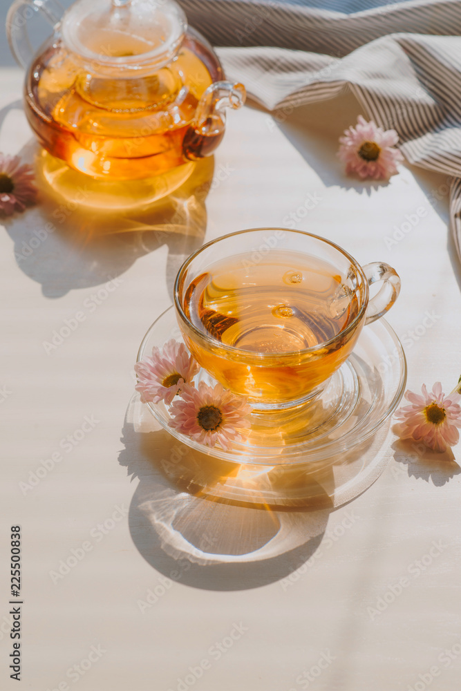 桌子上放着一杯草药洋甘菊茶。透明杯子里的洋甘菊茶和t上的洋甘菊花