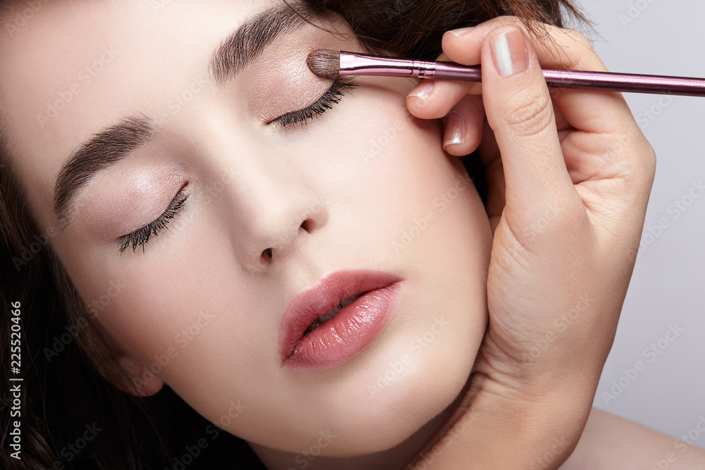 Make-up artist apply beauty makeup on the eyelids of a beautiful girl. Visagist with makeup brush in