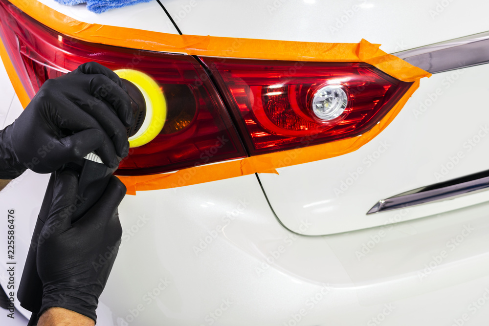 汽车抛光蜡工在抛光前用手在尾灯上涂保护胶带。抛光和