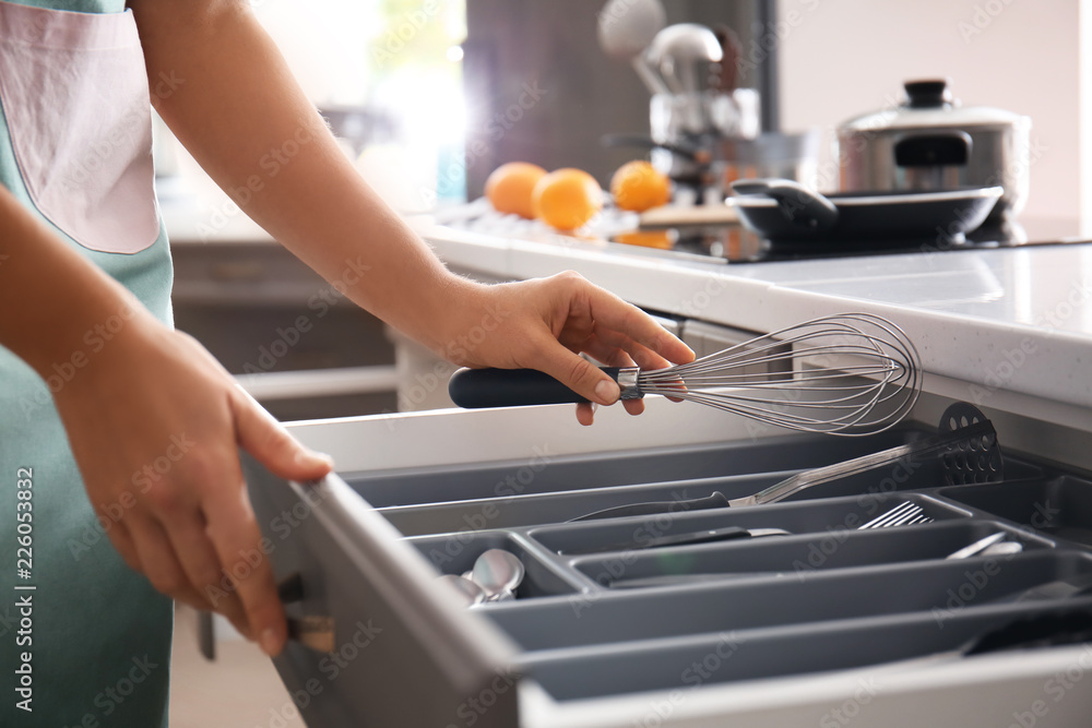 Woman putting whisk into kitchen drawer