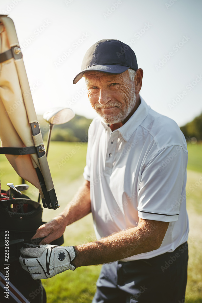 微笑的老人透过他的高尔夫球杆包看