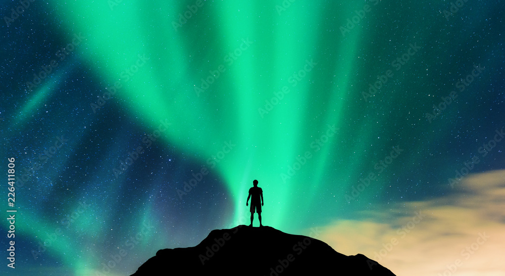 极光和独自一人站在山峰上的剪影。挪威罗弗敦群岛。极光博