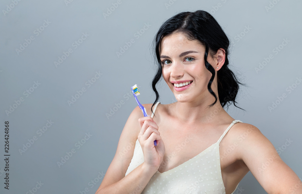 灰色背景下拿着牙刷的年轻女子