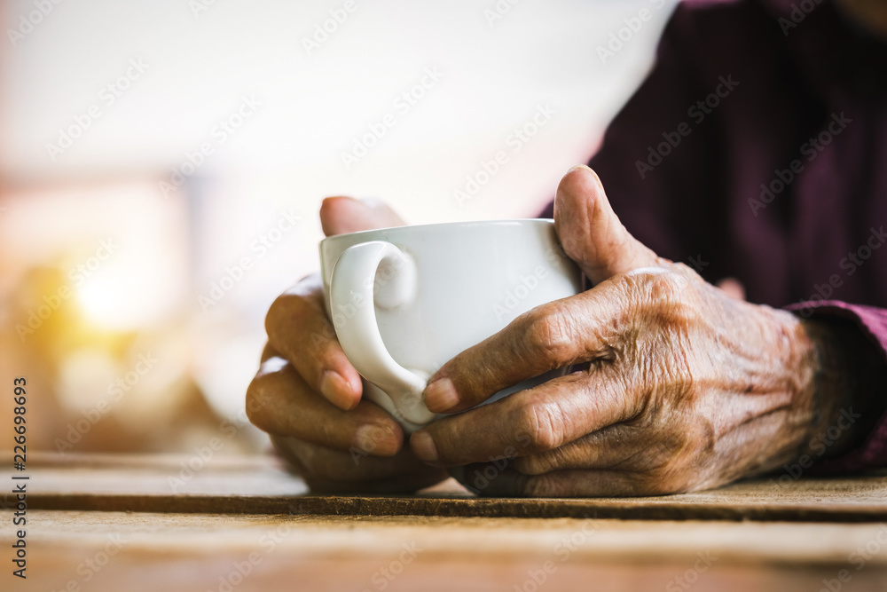 木头桌子上拿着一杯咖啡的老人的手。语调
