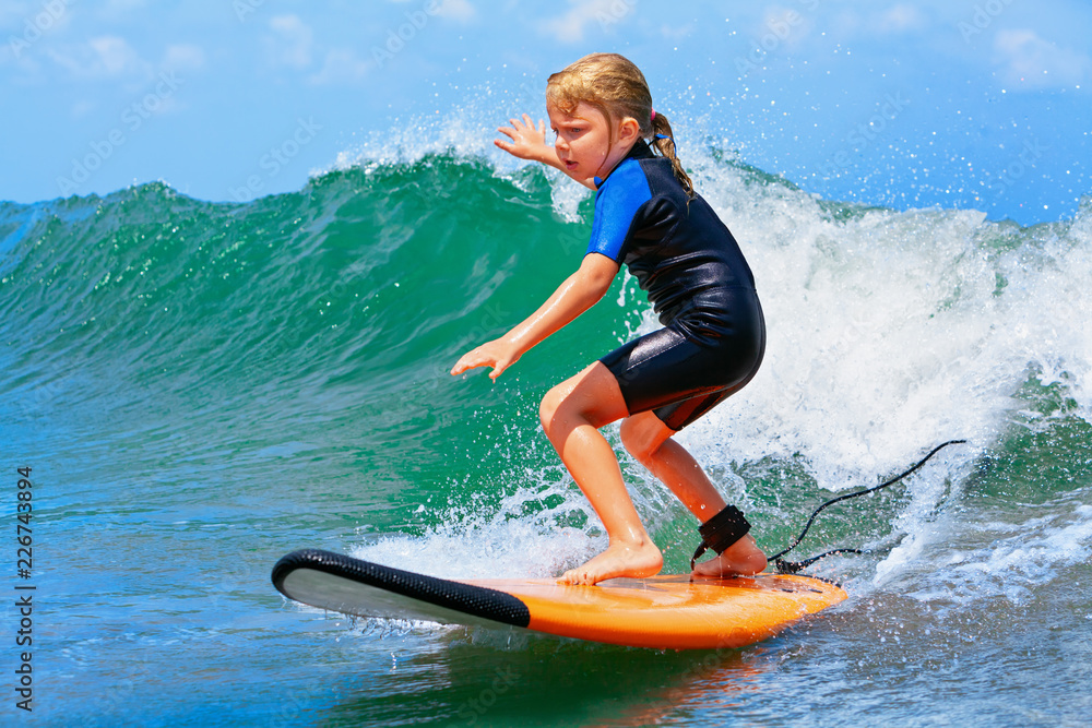 快乐的小女孩-年轻的冲浪者在冲浪板上冲浪，享受海浪的乐趣。活跃的家庭生活方式，孩子