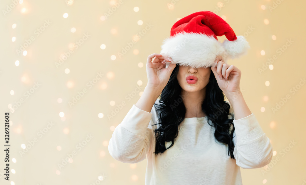 戴着圣诞帽的女人在闪亮的灯光背景下遮住了眼睛