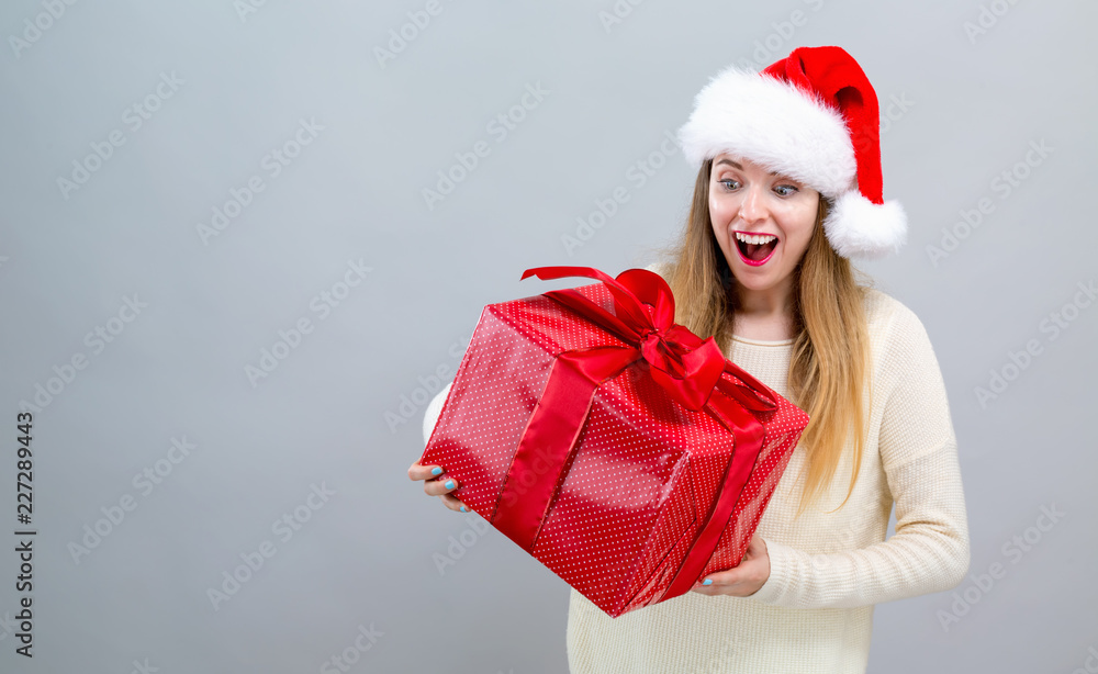 戴着圣诞老人帽的年轻女子拿着灰色背景的礼盒