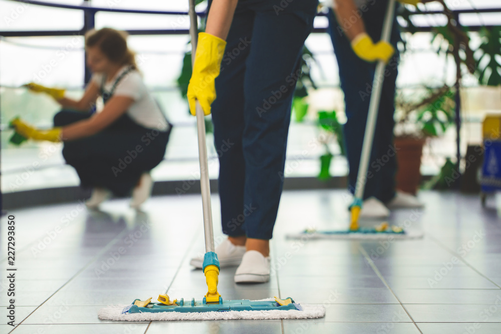 戴着黄色手套和拖把擦拭地板的专业清洁人员特写