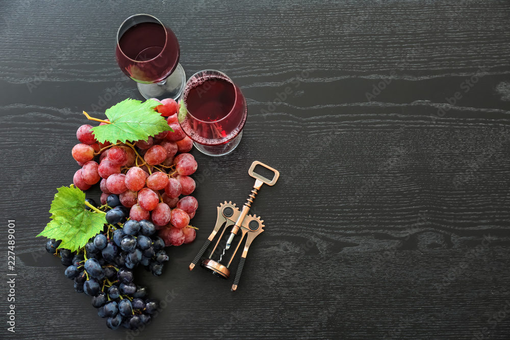 深色木桌上的一杯红酒、开瓶器和成熟的葡萄