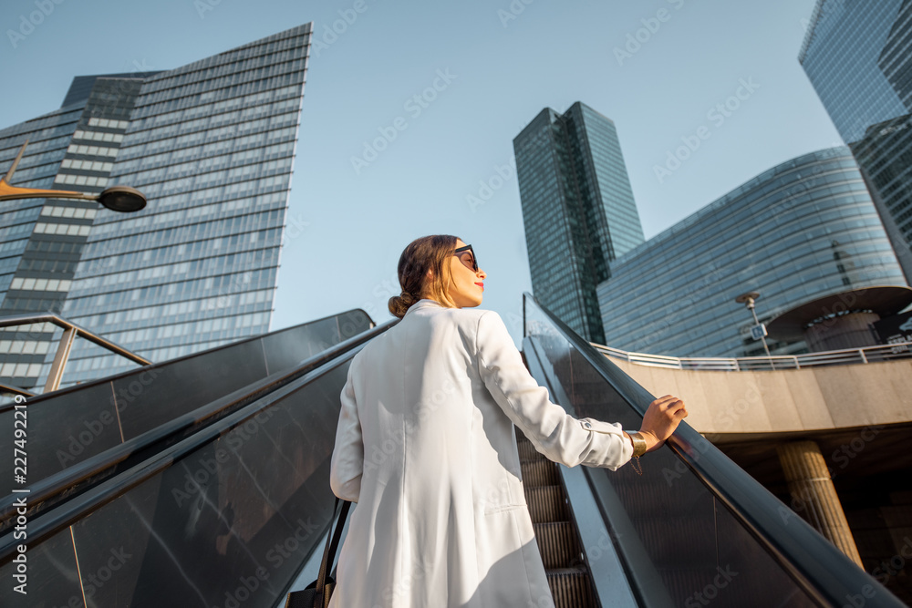 Stylish businesswoman in white suit going up on the escalator at the business centre outdoors with s