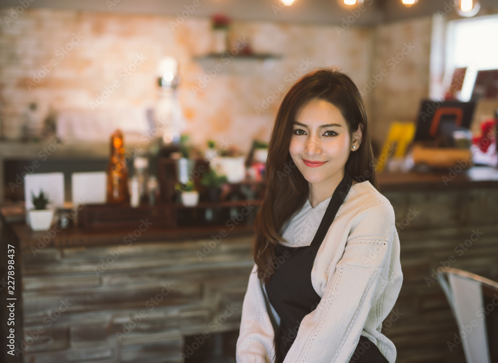 亚洲女服务员穿着围裙站在咖啡店里的肖像。