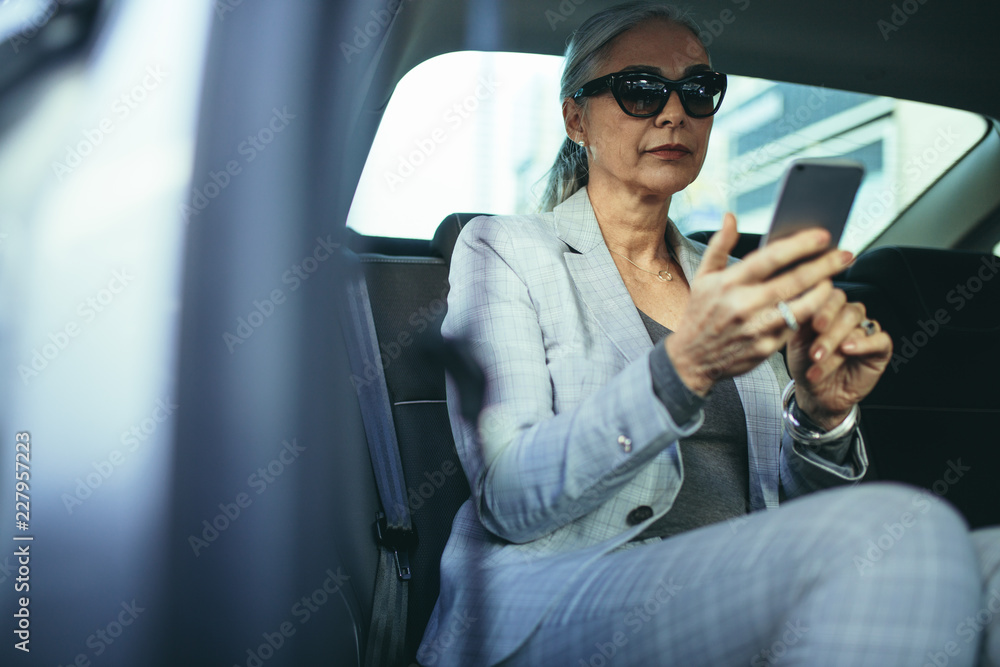 Senior businesswoman traveling by a car using smart phone