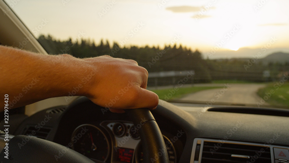 特写：日落时分驾驶时，无法辨认的人握着方向盘