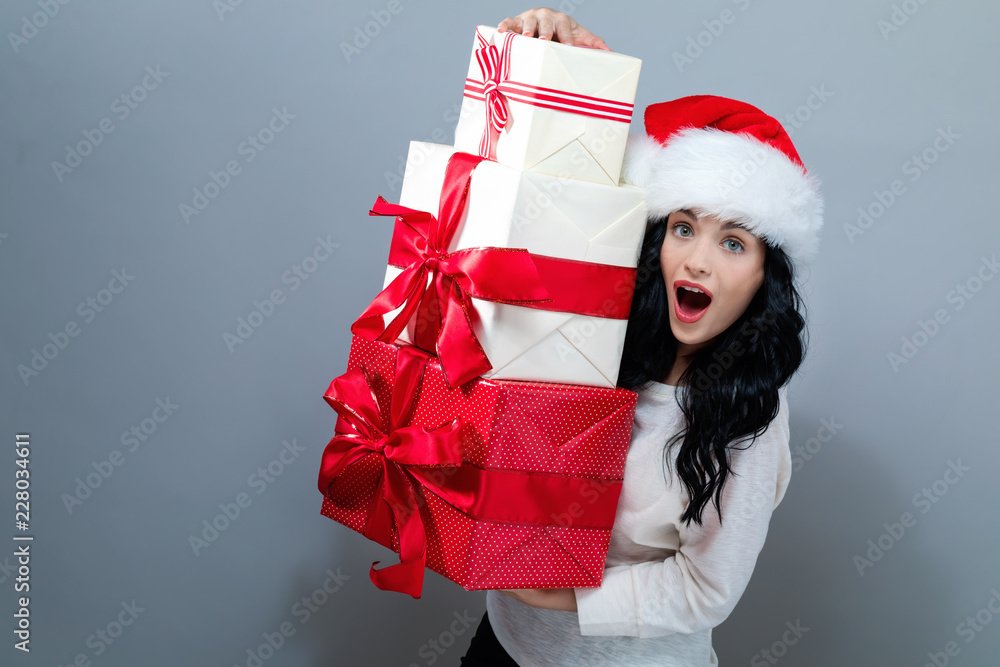 戴着圣诞老人帽的年轻女子在灰色背景下拿着礼盒