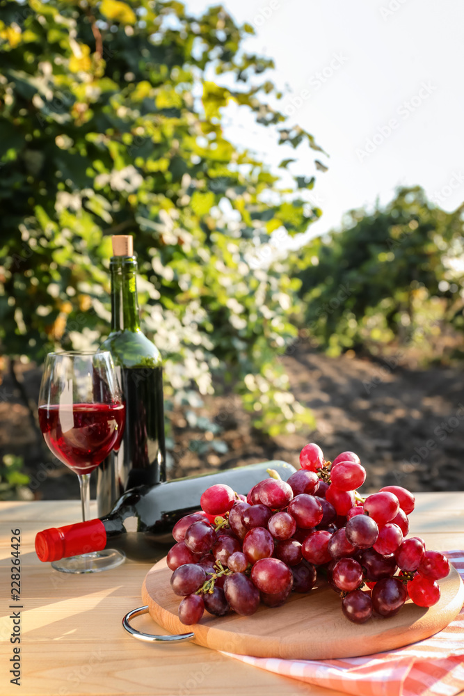 葡萄园木桌上摆放着一瓶瓶红酒的新鲜葡萄