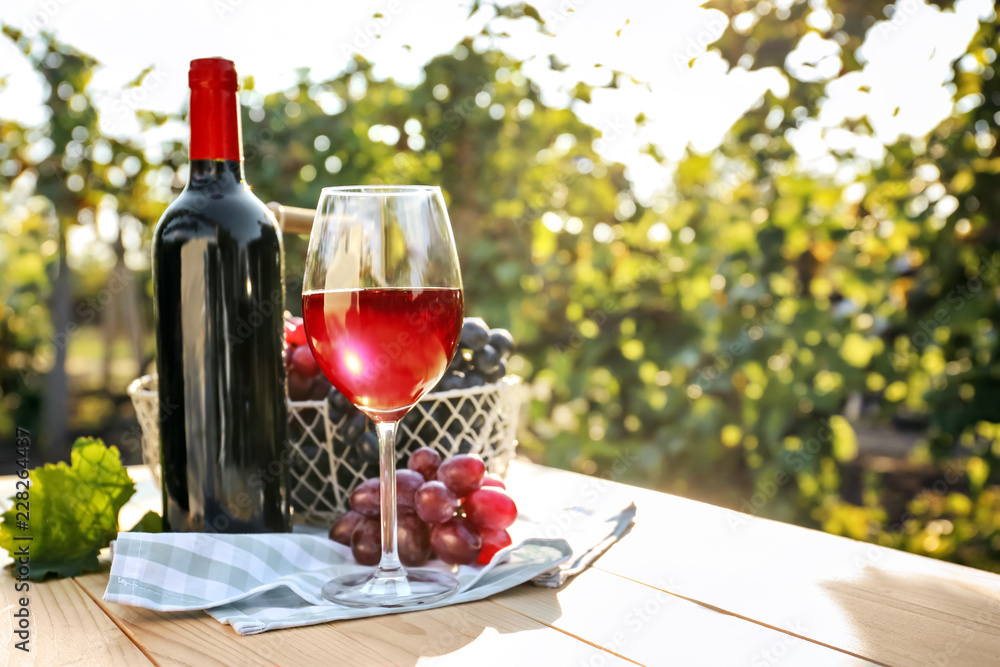 葡萄园木桌上放着一杯和一瓶新鲜葡萄的红酒