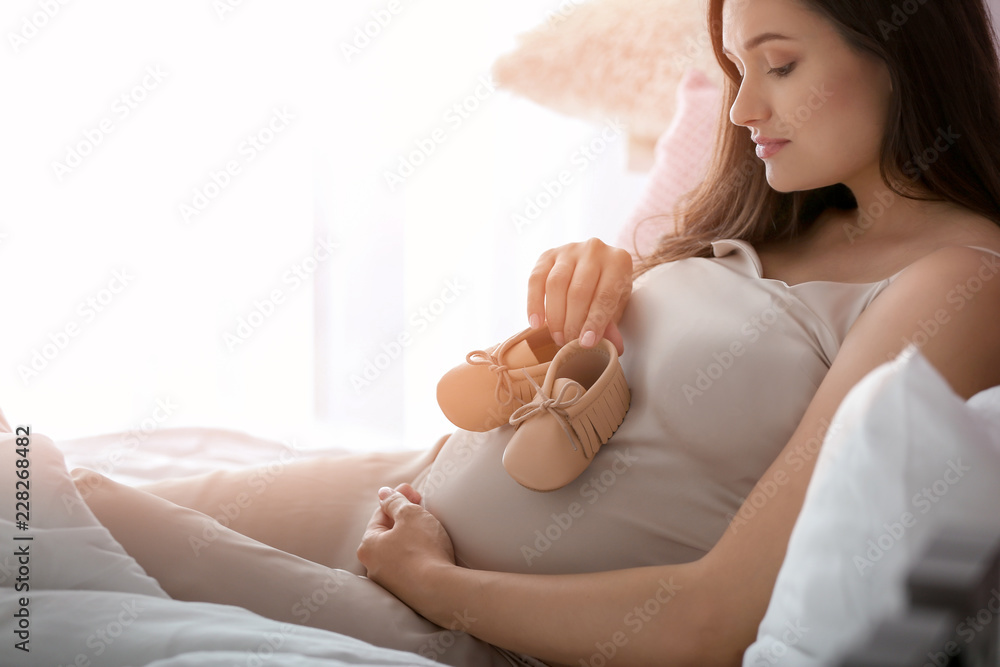 漂亮的孕妇在卧室里穿着婴儿靴
