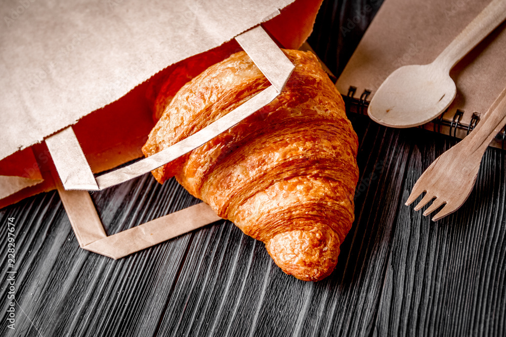 cup coffee and croissant in paper bag on wooden background