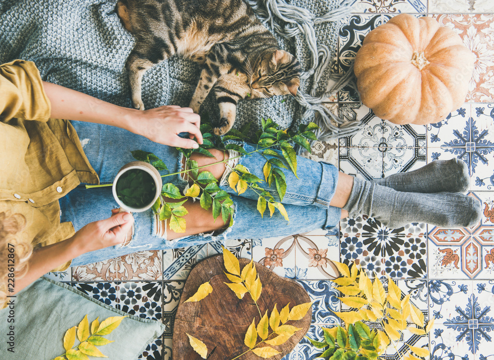 秋天或秋天的阳台喝茶时间。女性平躺在五颜六色的瓷砖地板上，喝着她