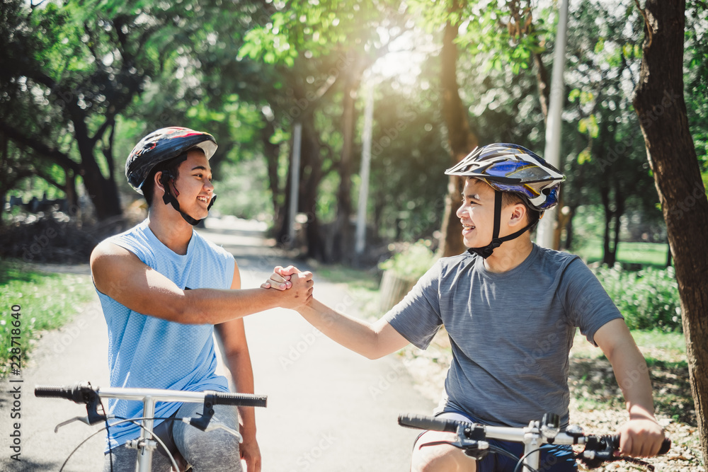 亚洲男孩和朋友夏天在户外绿色公园骑自行车/自行车，团队合作理念