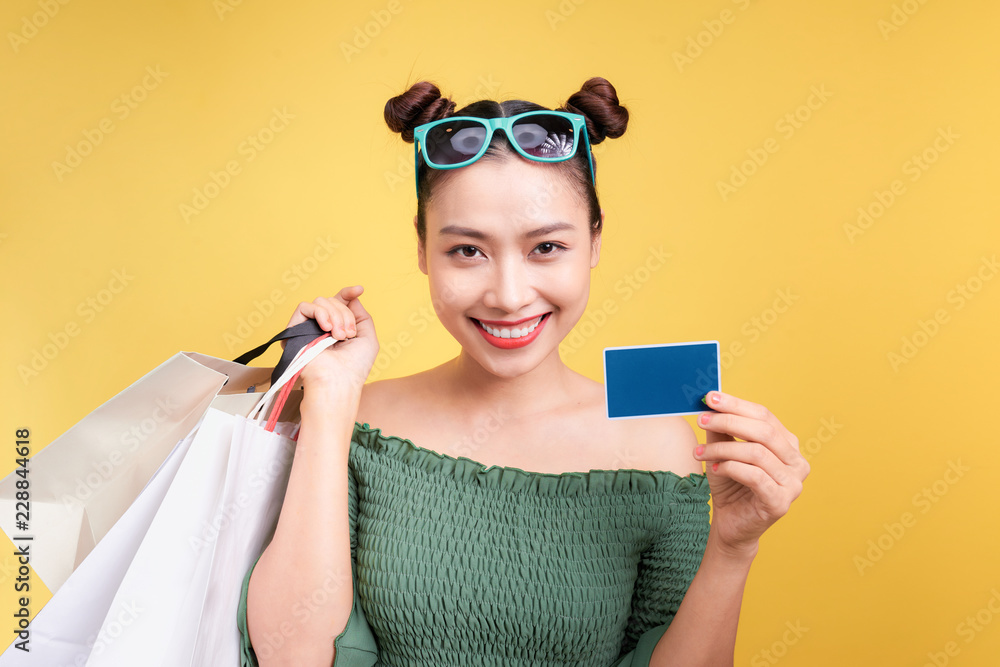 购物的亚洲女人拿着黄色背景的购物袋和信用卡