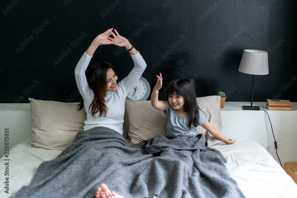 快乐的早晨时刻，带着女儿的家庭单身妈妈醒来，在床上一起伸展身体