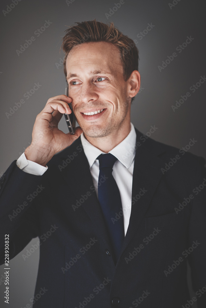 一个面带微笑的商人靠着灰色的背在手机上说话