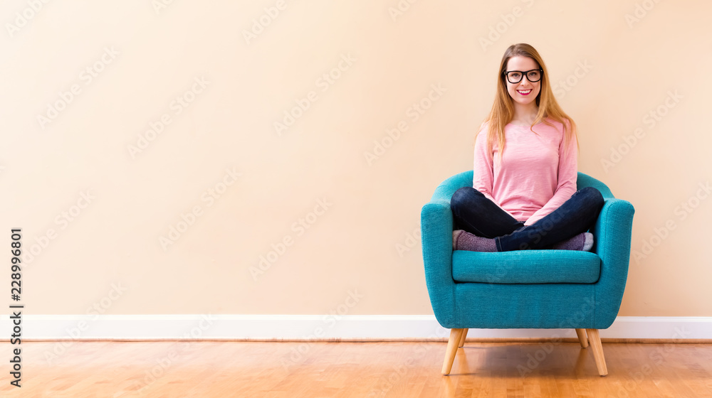 快乐的年轻女人坐在一把大椅子上，在一个敞开的大房间里微笑