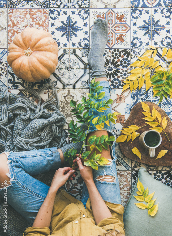 秋天或秋天的阳台喝茶时间。女性平躺在五颜六色的瓷砖地板上，手里拿着掉落的l