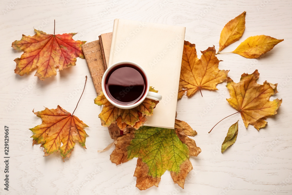 由一杯美味的热葡萄酒、笔记本和浅色背景的秋叶组成