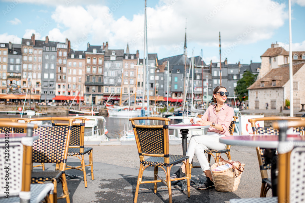一名年轻女子坐在法国洪弗勒老城港口附近的户外咖啡馆里享受咖啡