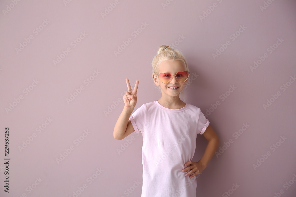 可爱的小女孩穿着t恤，在彩色背景上展示胜利手势