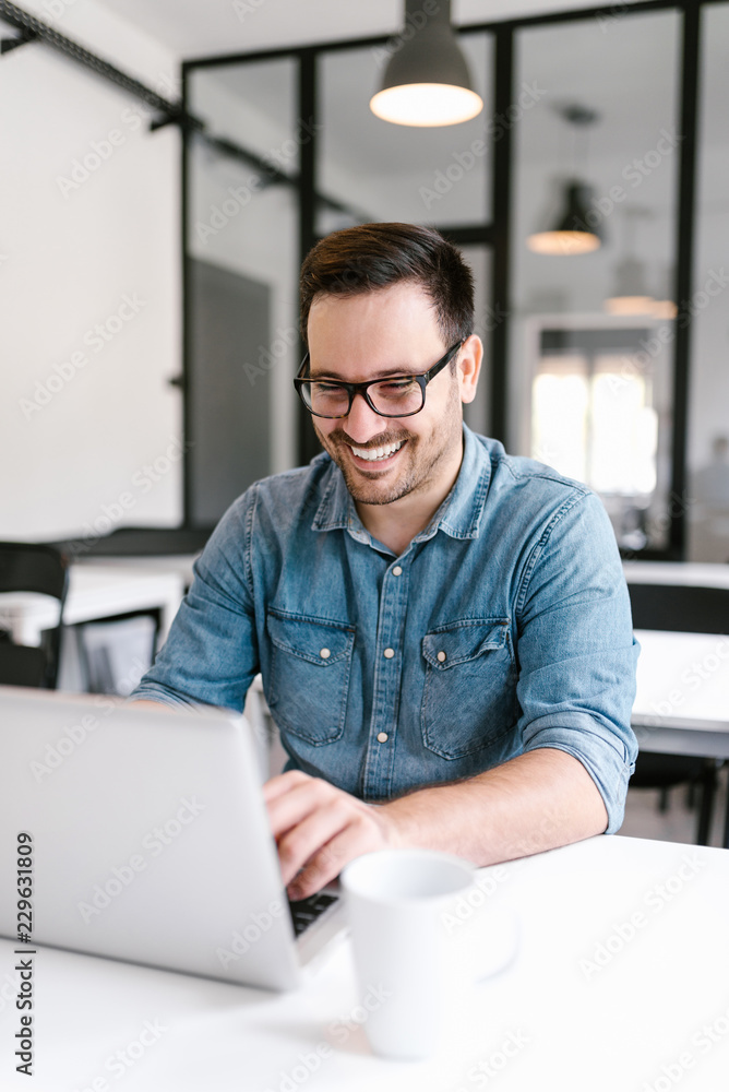 微笑的年轻人在现代办公室里使用笔记本电脑。