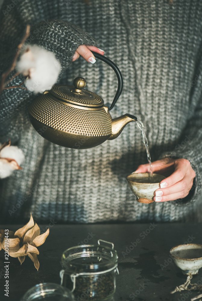 茶道。穿着灰色保暖针织冬衣的女人从金色铁壶里倒绿茶