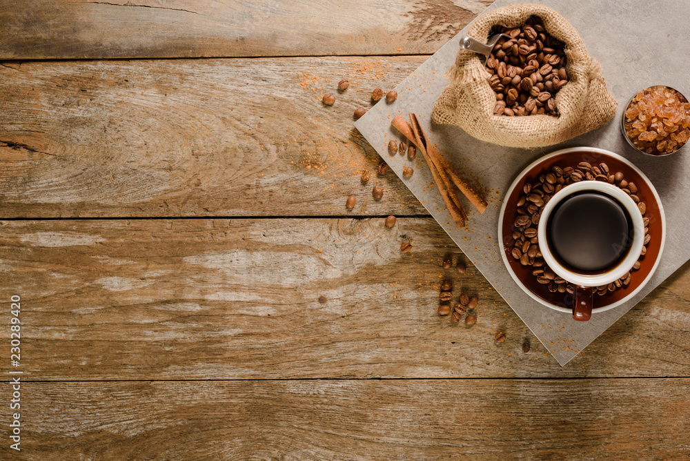 一杯美式咖啡的俯视图，木质背景地板上有咖啡豆袋、糖和肉桂